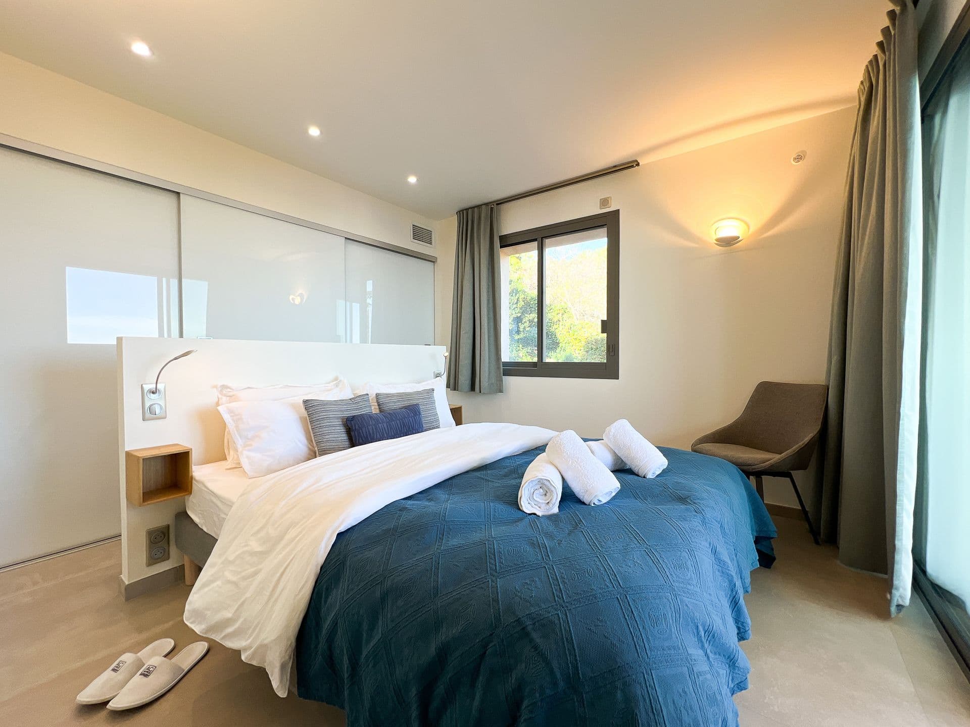 Bedroom with navy linens and a seating nook beside the sea-facing window