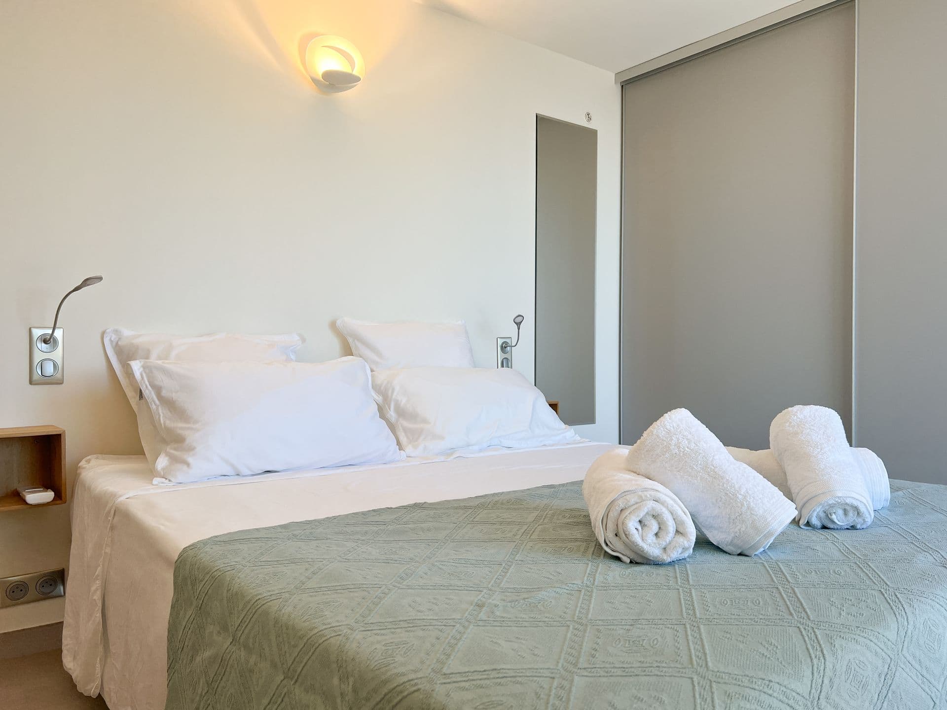Bedroom with sage green linens and a rolled-towel welcome on the bed