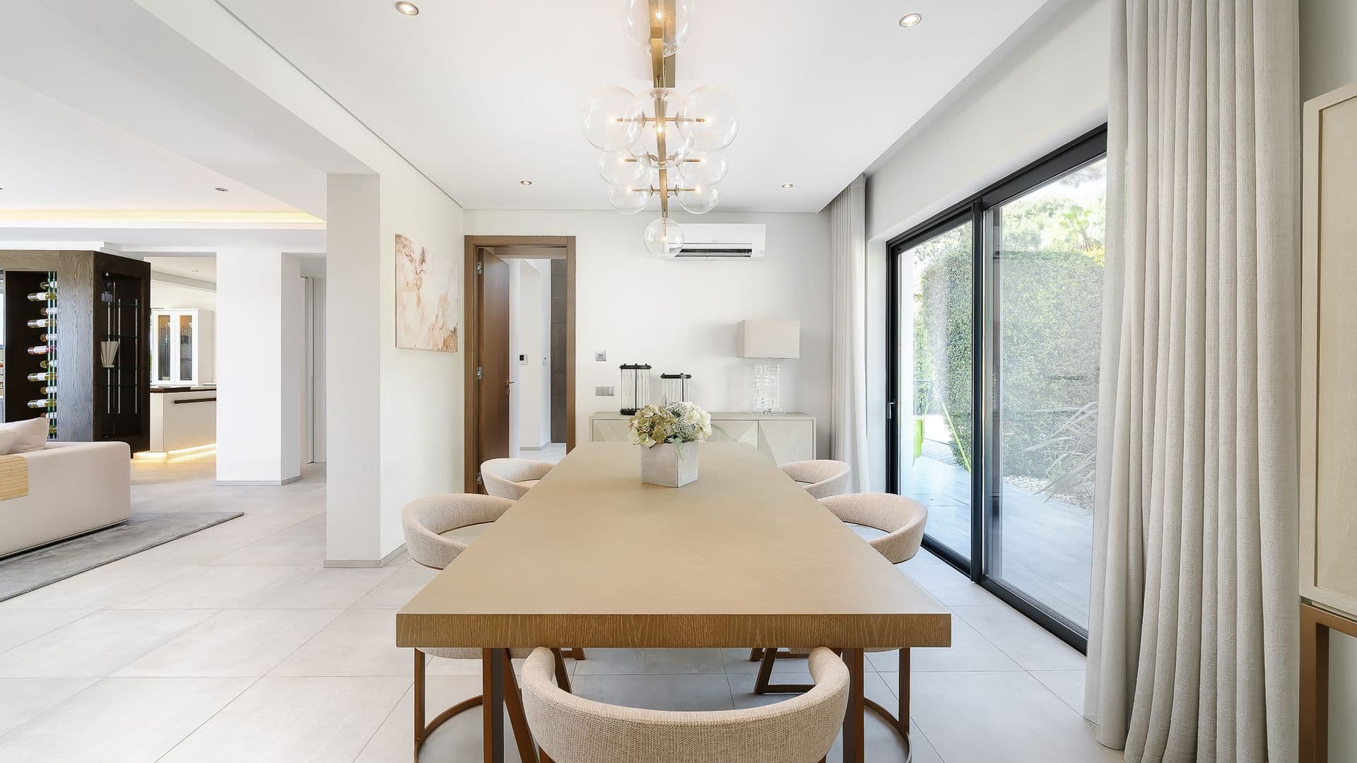 Long dining table beside floor-to-ceiling glass doors framing the garden