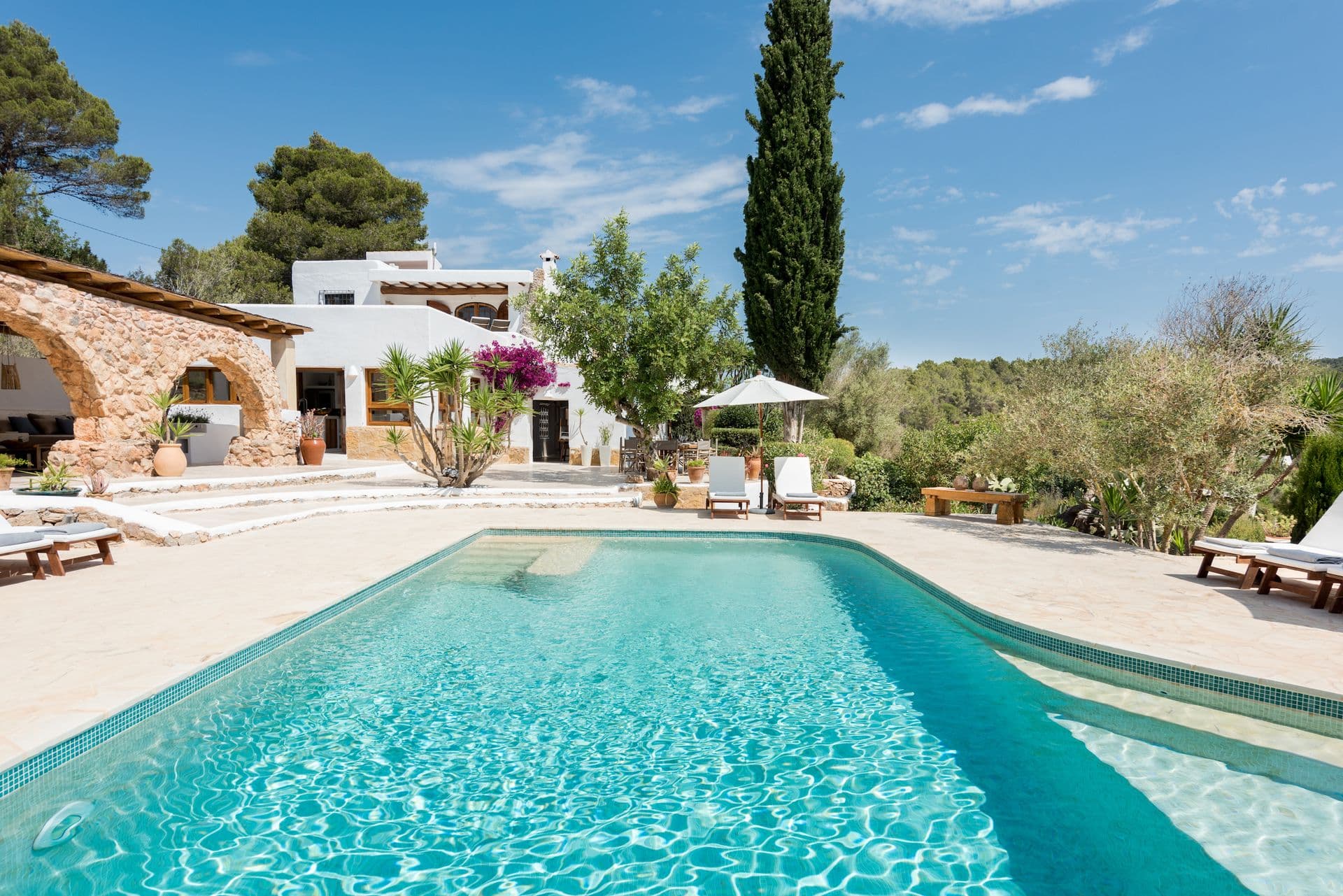 Long swimming pool with sun loungers beside the finca and cypress trees