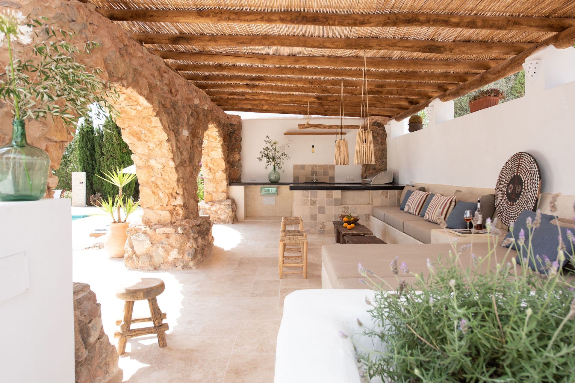 Covered outdoor kitchen and lounge area under a stone archway with woven pendant lights