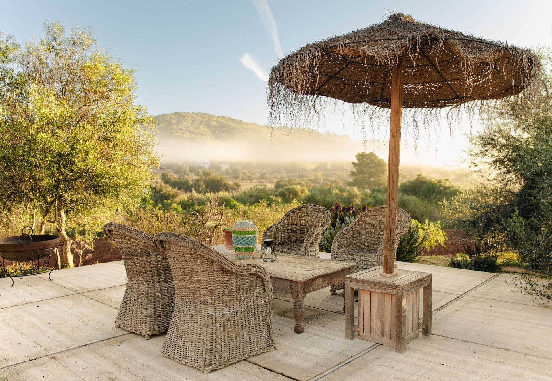 Terrace with wicker chairs and a thatched parasol overlooking hills at golden hour