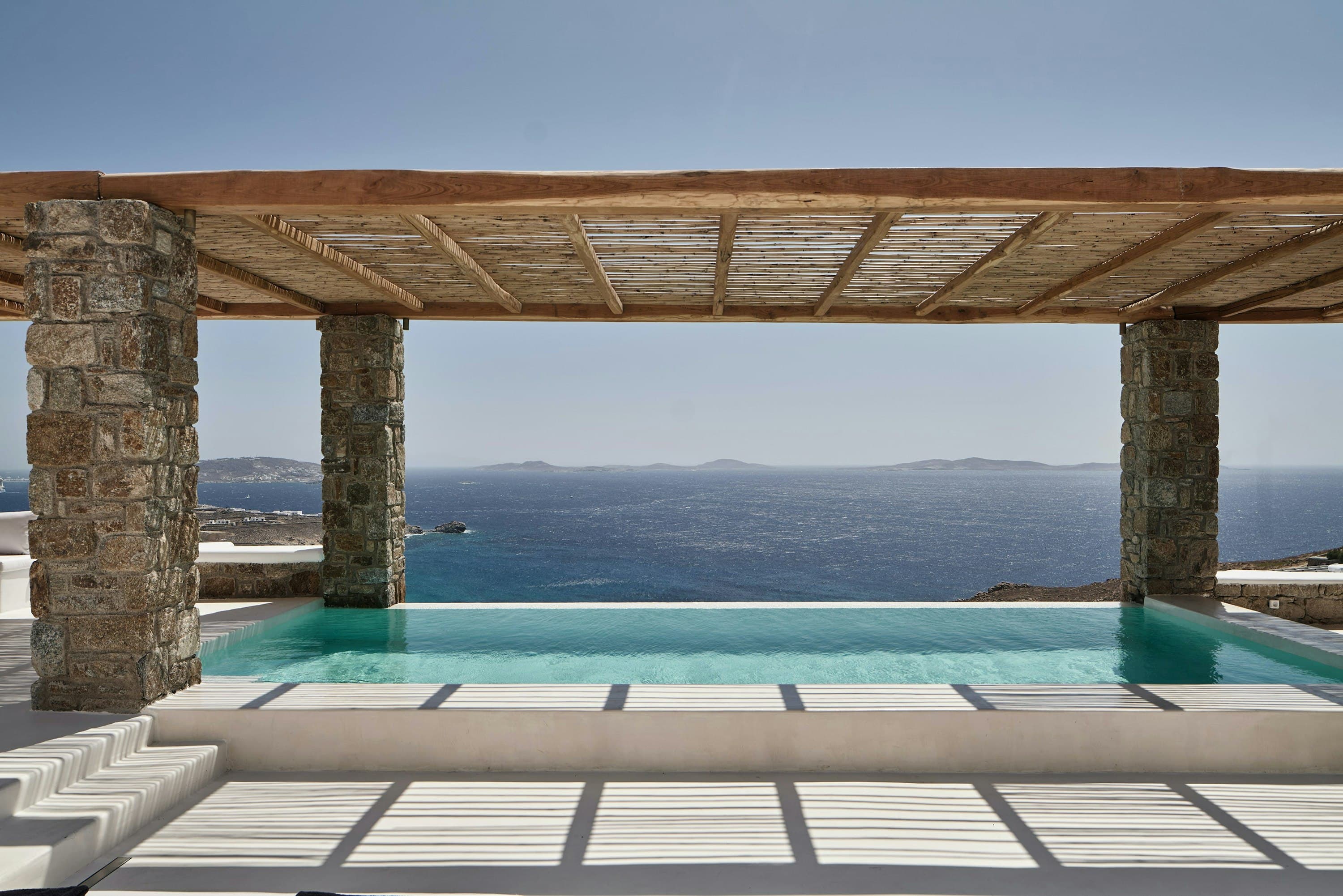 Bohemian Bay Retreat infinity pool with stone columns overlooking the Aegean Sea, Mykonos, Greece