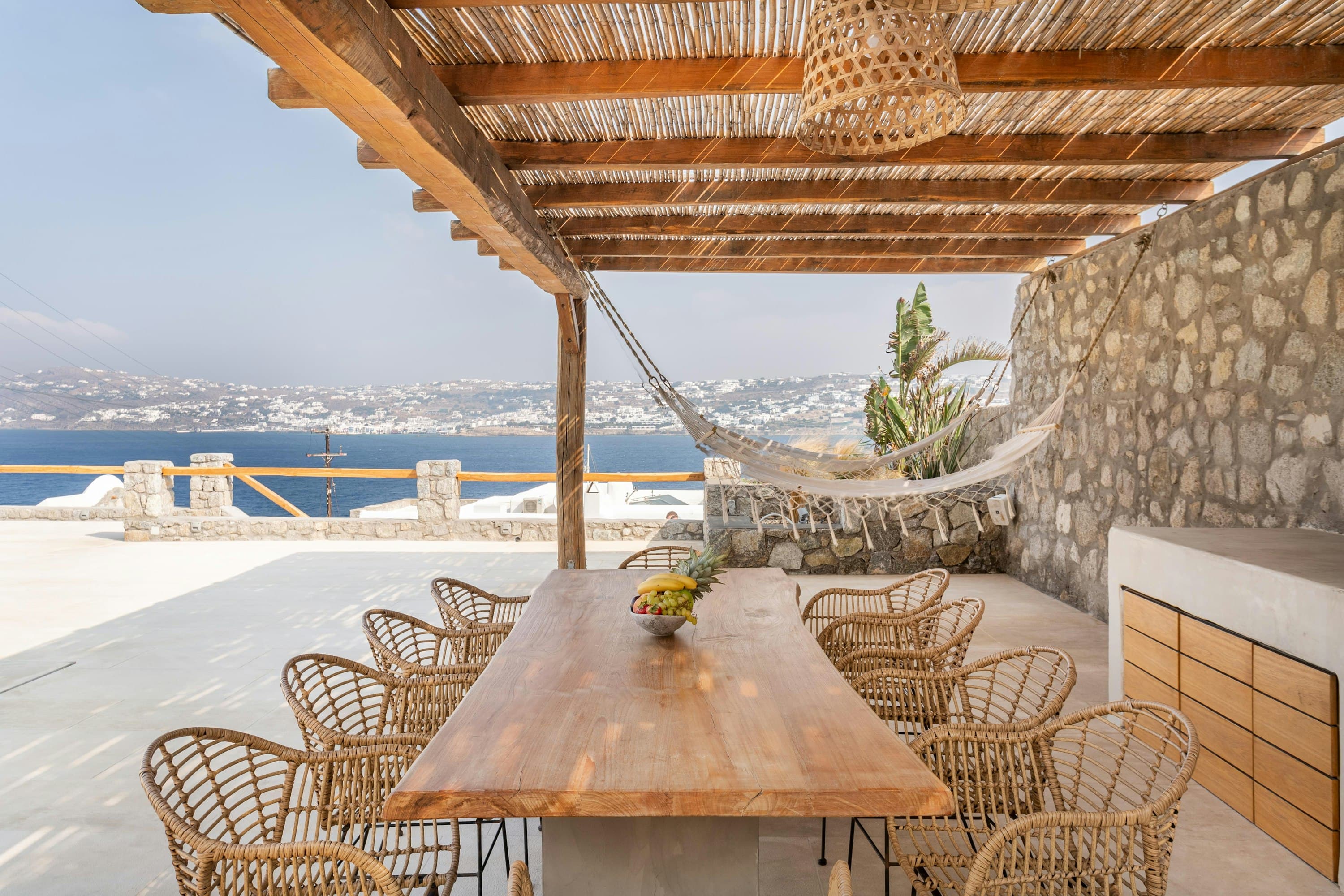 Just Fly, Don't Worry shaded terrace with natural wood dining table overlooking the Aegean, Mykonos, Greece